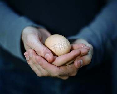 一位年轻男子小心翼翼地拿着一个鸡蛋