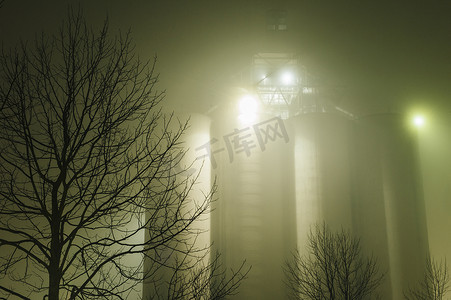 黑大气背景摄影照片_美国华盛顿州西雅图夜间工业储油罐和树木轮廓的迷雾景观