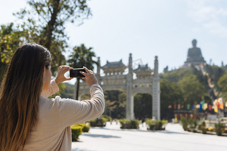 年轻女游客在用智能手机拍摄香港大屿山宝莲寺天坛佛像中国