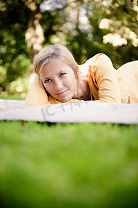 一名女子躺在公园里的毯子上