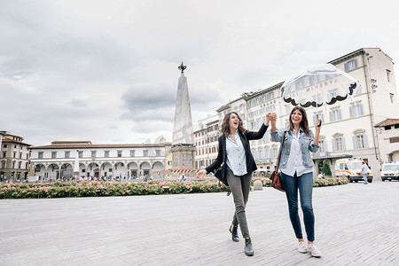 下着雨摄影照片_意大利托斯卡纳佛罗伦萨圣玛丽亚·诺维拉广场女同性恋夫妇打伞嬉戏手牵手微笑