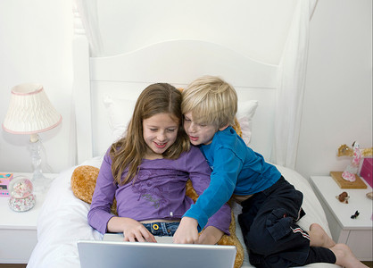 男孩和女孩在床上看着笔记本电脑