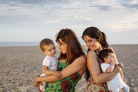 站在海滩上抱着婴儿和蹒跚学步的孩子的母亲