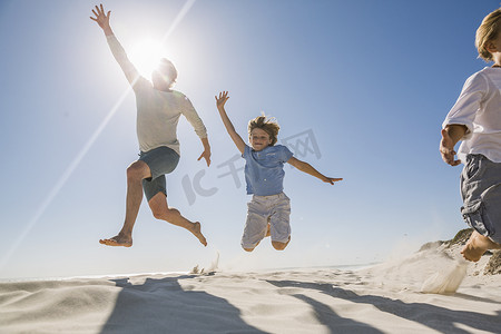 光斑效摄影照片_海滩上的父子俩高举双臂在半空中跳跃