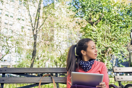 一名年轻女子在公园长椅上一边看一边使用数字平板电脑