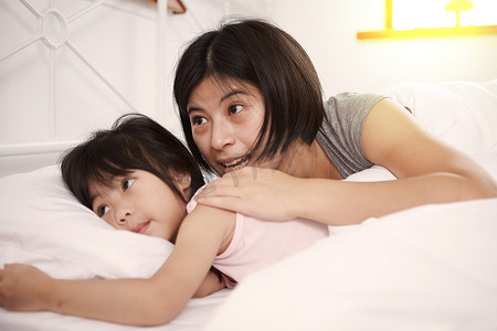 松鹤中国风名片摄影照片_年轻的中国母亲和女儿一起躺在家里的床上