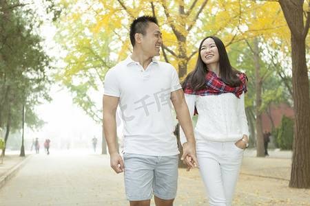 北京中国一对年轻夫妇在秋日绿树成荫的公园里散步