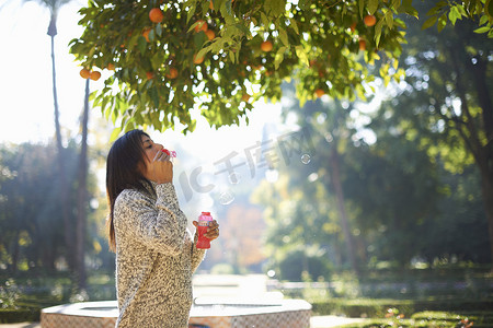 西班牙塞维利亚成熟女子在橘子树下吹泡泡的侧视