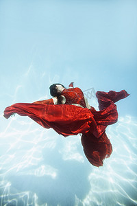 一名女子穿着红色连衣裙披着红色布料漂浮在水下