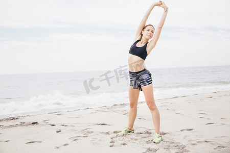 中年妇女站在海滩上双手举过头顶伸展身体的肖像