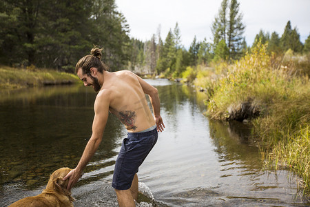 抱胸的男人摄影照片_美国内华达州太浩湖一名年轻男子抱着狗在河里划水