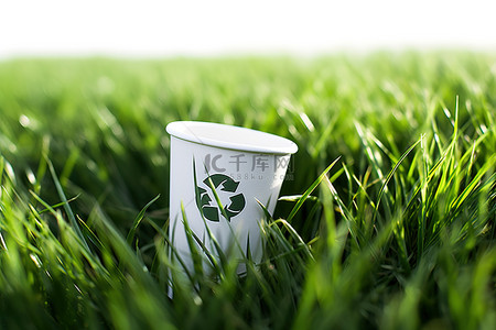 环保标志纸杯背景图片_一个带有回收标志的纸杯被放置在草丛中
