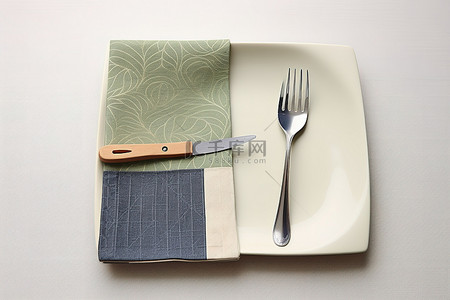 叉子叉着芒果背景图片_一张方形餐巾，上面放着盘子和叉子，下面还有一张布餐巾