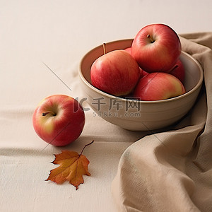 医美回馈感恩展架背景图片_四个红苹果放在一个小碗里，放在铺满秋叶的桌子上