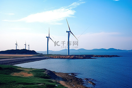 风力涡轮机矗立在海洋旁边，背景是水和陆地