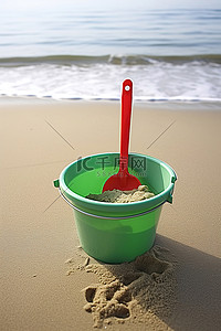 一个绿色的桶，上面有一个红色的勺子，坐在沙子上