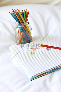 白色床上有彩色铅笔的笔记本