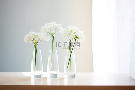 桌子前放着一排三个小花瓶，上面开着白花