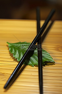黑色筷子背景图片_带叶子的黑色和绿色筷子坐在木桌上