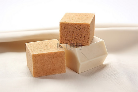 丝瓜水嫩背景图片_三块棕色肥皂，形状像白布上的肥皂块