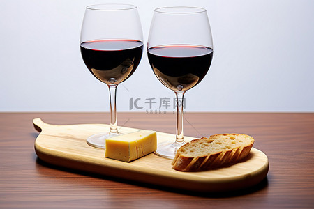 木板上放着两个红酒杯，上面有奶酪和意式烤面包