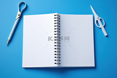 蓝色墙上有剪刀和夹子的空白笔记本
