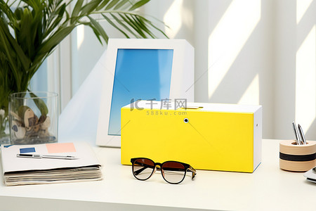 蓝色太阳镜背景图片_白纸活页夹装在黄色和蓝色三角形盒子里，上面有两个太阳镜和眼镜，放在白色桌子上
