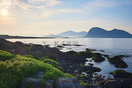 太阳在岩石海滩的海洋上升起，背景是山脉