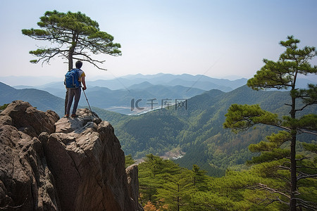 美团美团背景图片_一个带着攀爬架的年轻人站在岩石顶上，周围的景色很美