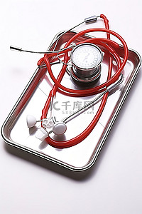 白色背景银托盘内的红色听诊器和血压计