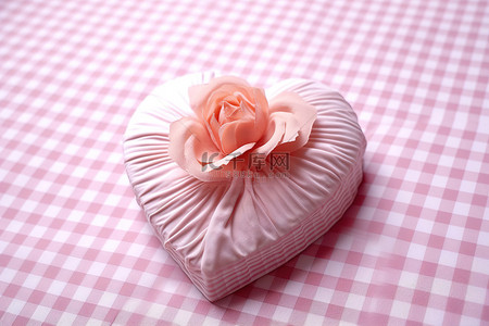 装饰花朵心形背景图片_一朵心形的粉红色花朵坐落在白色格子桌布上