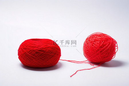 一个红色的毛线球坐在一个白色的毛线球旁边