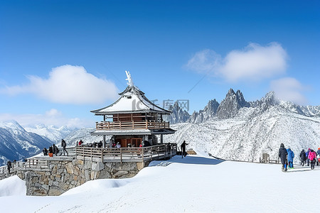 一座被雪覆盖的大山，有一个木制凉亭，旁边站着穿着滑雪服的人