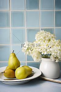 水果蓝水果背景图片_蓝白瓷砖墙上放着一个白盘和一碗梨，上面有花