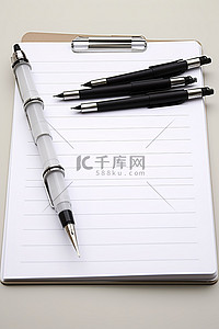 钢笔的笔尖背景图片_白色剪贴板上的四支笔尖笔和一个空记事本
