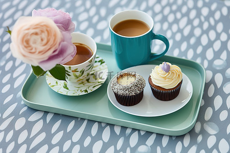拿鲜花的背景图片_一杯茶和一杯咖啡，蓝色托盘上放着鲜花，上面有两个纸杯蛋糕