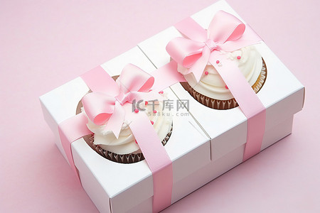 白色盒子里有两个纸杯蛋糕，上面有粉色蝴蝶结