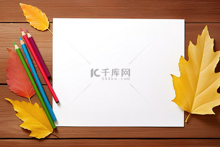 桌上彩色铅笔旁边有五颜六色的叶子和一张空白纸