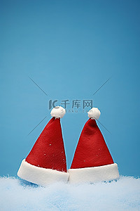 蓝色帽子冬天背景图片_蓝色背景上的两顶圣诞老人帽子