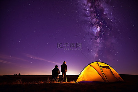 夜晚帐篷背景图片_晚上，两个人站在黑暗中看着帐篷上方的星星