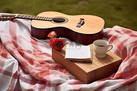 一把木吉他坐在毯子上，旁边是一杯书和一杯爪哇咖啡