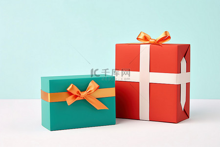 礼盒一堆背景图片_白色表面上一张卡片旁边的两个红色和绿松石色礼盒