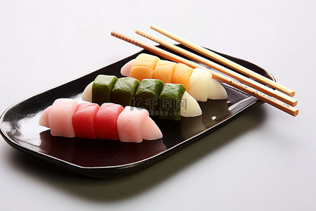 红色和黄色的筷子，上面有寿司，还有一个黑色的盘子