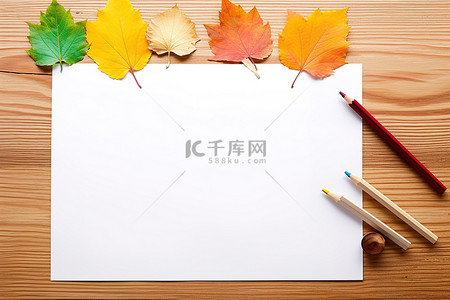 背景银杏背景图片_桌上彩色铅笔旁边有五颜六色的叶子和一张空白纸