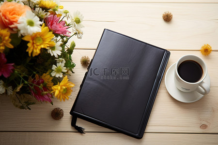 白色木桌上的黑色笔记本，上面有鲜花和咖啡