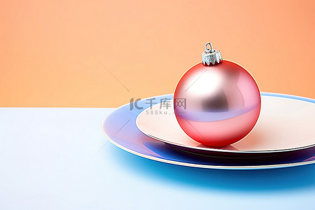 圣诞橙色背景图片_白色底座上橙色和蓝色盘子中的两个圣诞装饰品