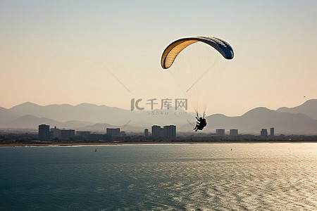 滑翔伞手绘背景图片_在海洋附近滑翔伞，背景是山脉