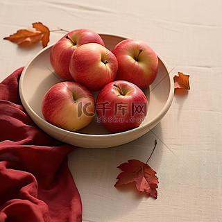 四个红苹果放在一个小碗里，放在铺满秋叶的桌子上