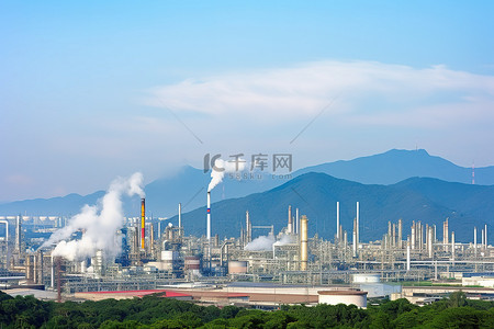 石化工厂照片背景图片_神户石化厂冒出烟雾，背景是山脉和树木