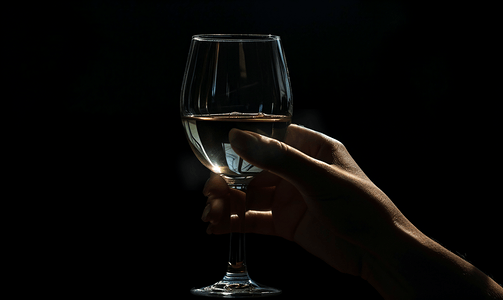 在黑暗中握着酒杯的女性的手